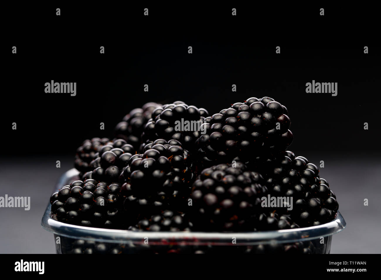 Photo of blackberry in plastic container on empty black background. Stock Photo