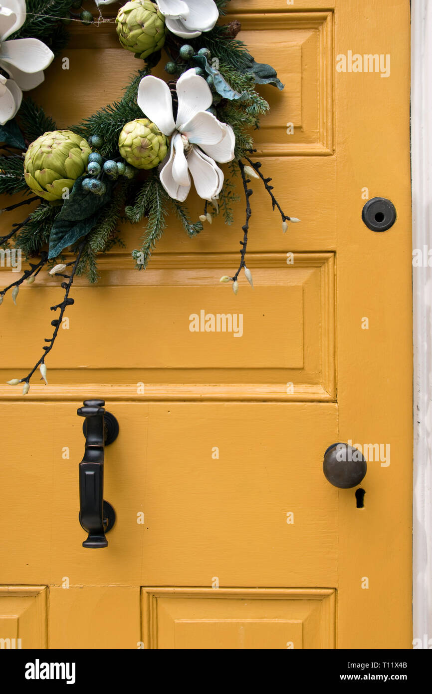 A wreath of flowers decorates the brightly painted door of a brick Colonialera townhouse in New