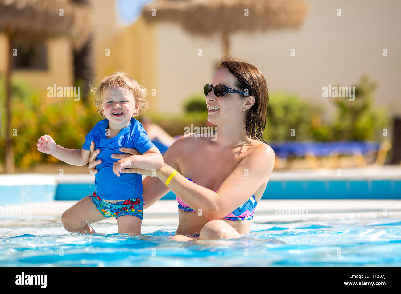Mother and baby in swimming pool. Parent and child swim in a tropical resort. Summer outdoor activity for family with kids. Vacation and traveling wit Stock Photo