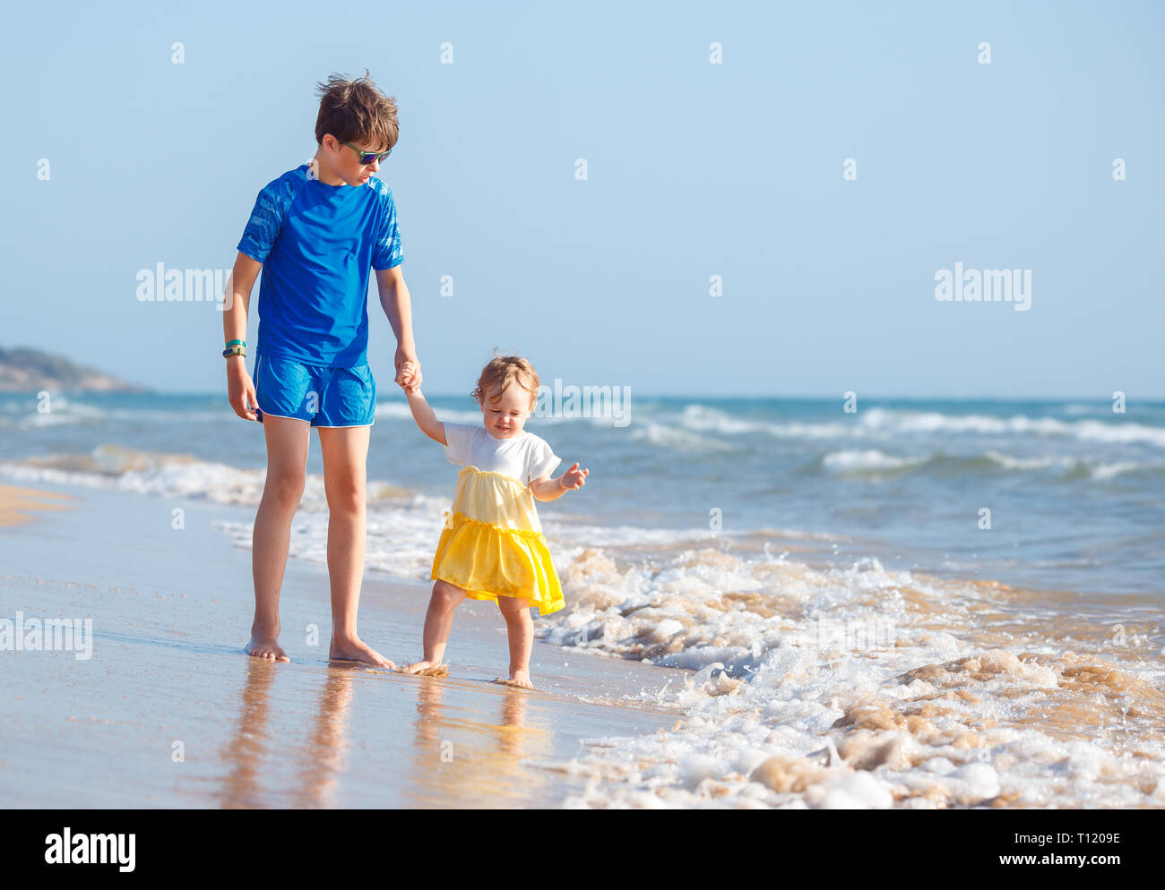 Kids playing on tropical beach. Big brother together with his little sister at sea shore at sunset. Family summer vacation. Children play with water.  Stock Photo