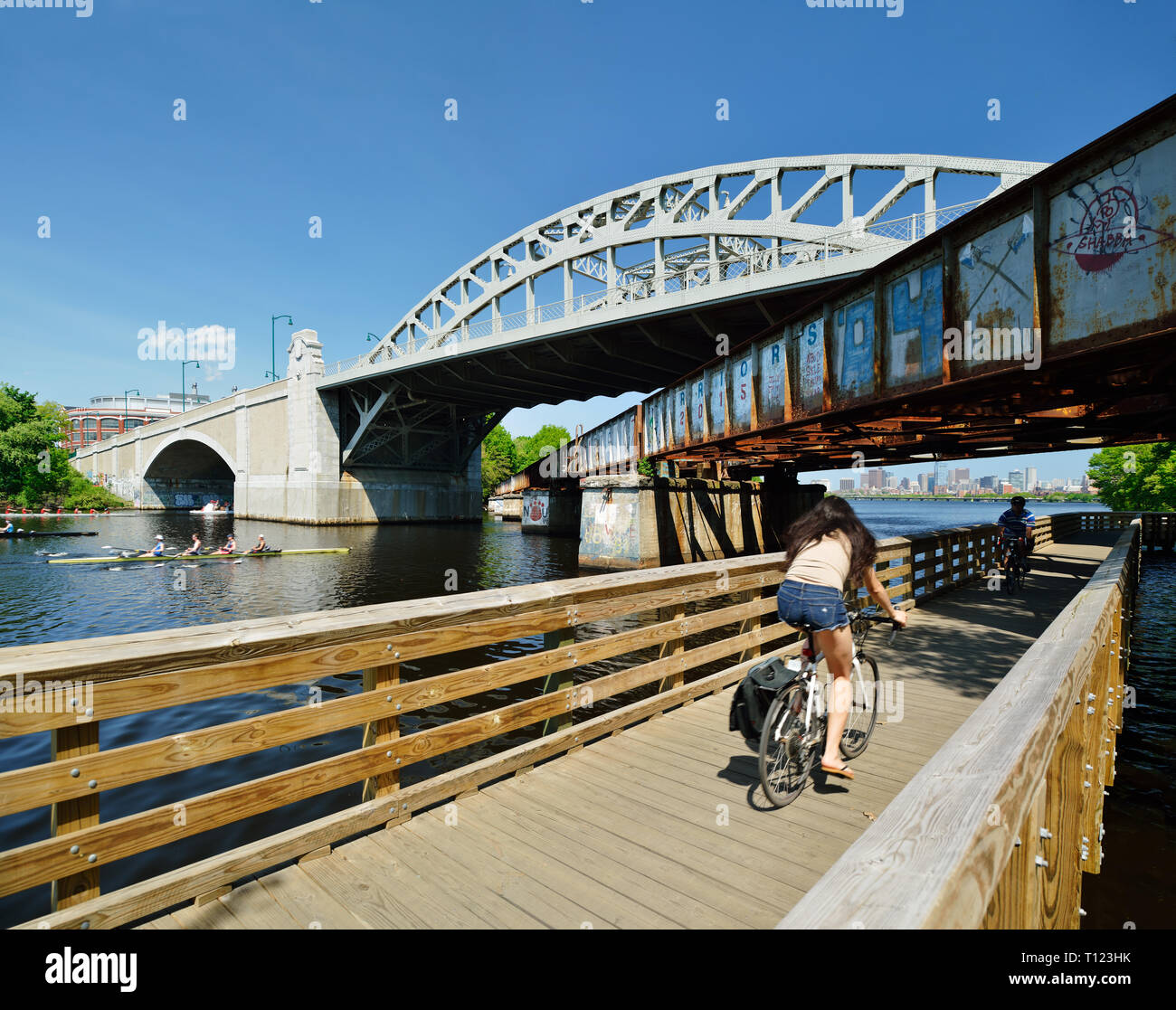 BU Bridge, old railroad and bike path on Charles River. People commuting and rowing, Boston city skyline in background. Massachusetts, USA Stock Photo