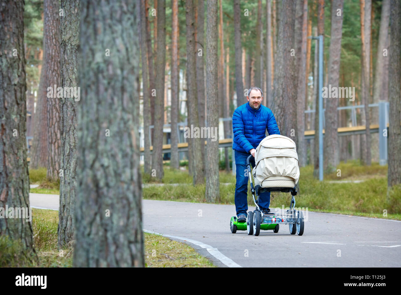 A young father on gyro scooter board with a stroller walks through the autumn park Stock Photo