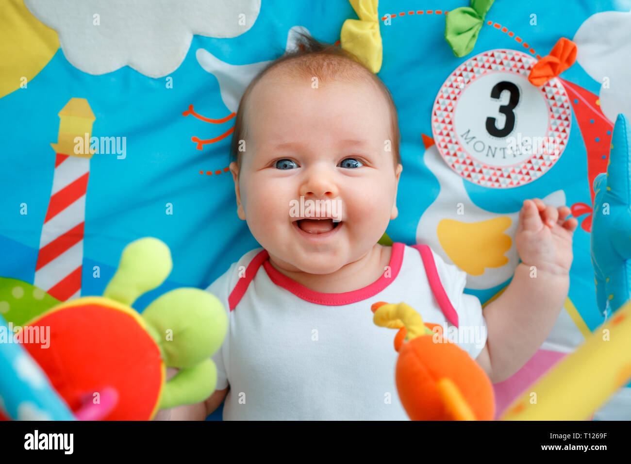 Adorable baby girl having fun with toys on colorful play mat. Happy healthy kid playing on the floor Stock Photo