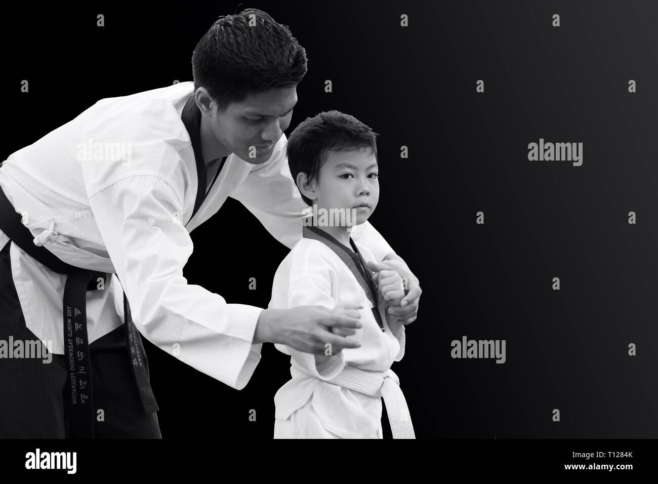 Taekwondo master black belt teaching kid to fight guard on black background Stock Photo