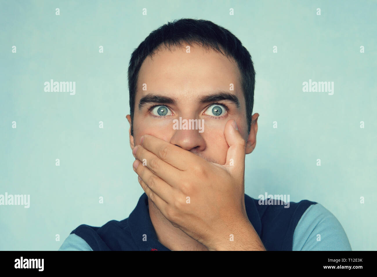 Frightened handsome male covers mouth as tries to stop talking, wears