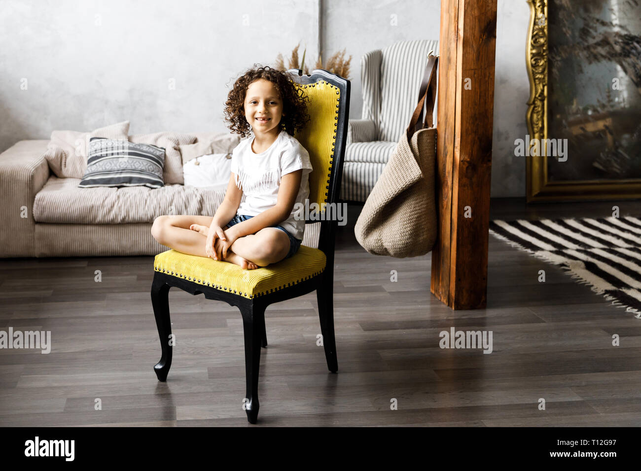 A pretty cute little girl with curly hair sitting on the chair and ...