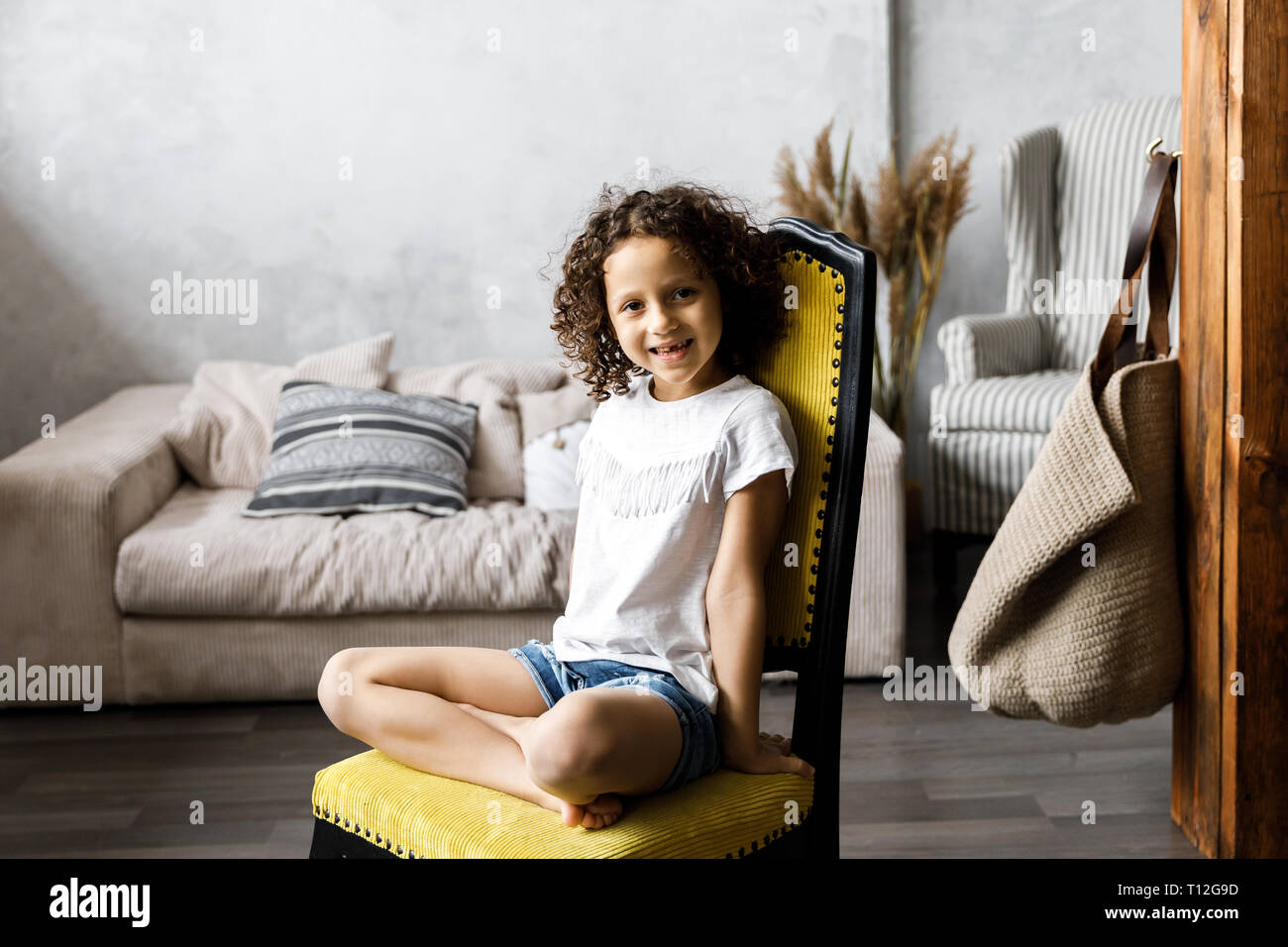 A pretty cute little girl with curly hair sitting on the chair and ...