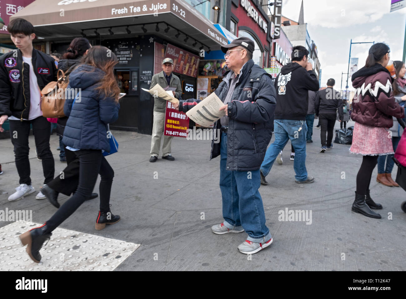 A man on Main st. & Roosevelt Ave. in Chinatown hands out Chinese language flyers. In Flushing, Queens, New York. Stock Photo