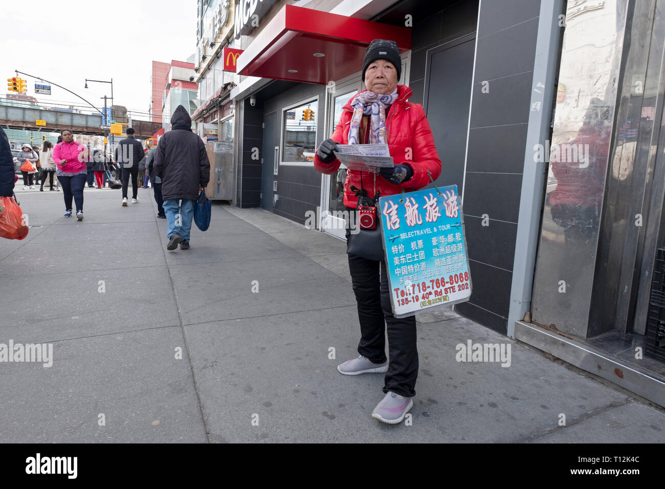 A woman on Main st. in Chinatown hands out Chinese language flyers for Selectravel & Tour. In Flushing, Queens, New York City. Stock Photo