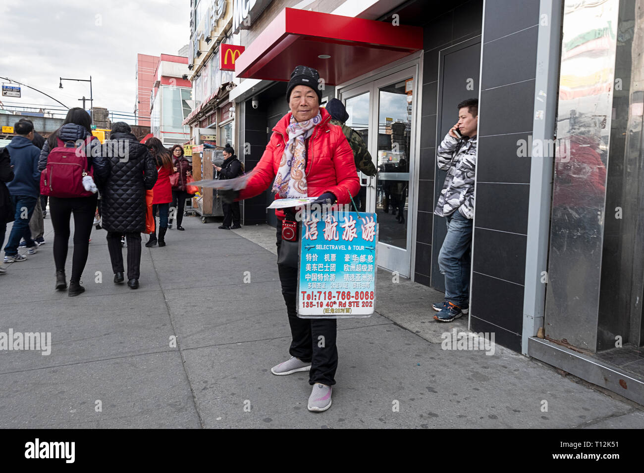 A woman on Main st. in Chinatown hands out Chinese language flyers for Selectravel & Tour. In Flushing, Queens, New York City. Stock Photo