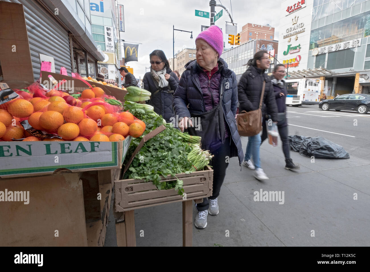 An older Chinese American woman shops for fruits & vegetables on a winter afternoon. In Chinatown, Flushing, Queens, New York City. Stock Photo