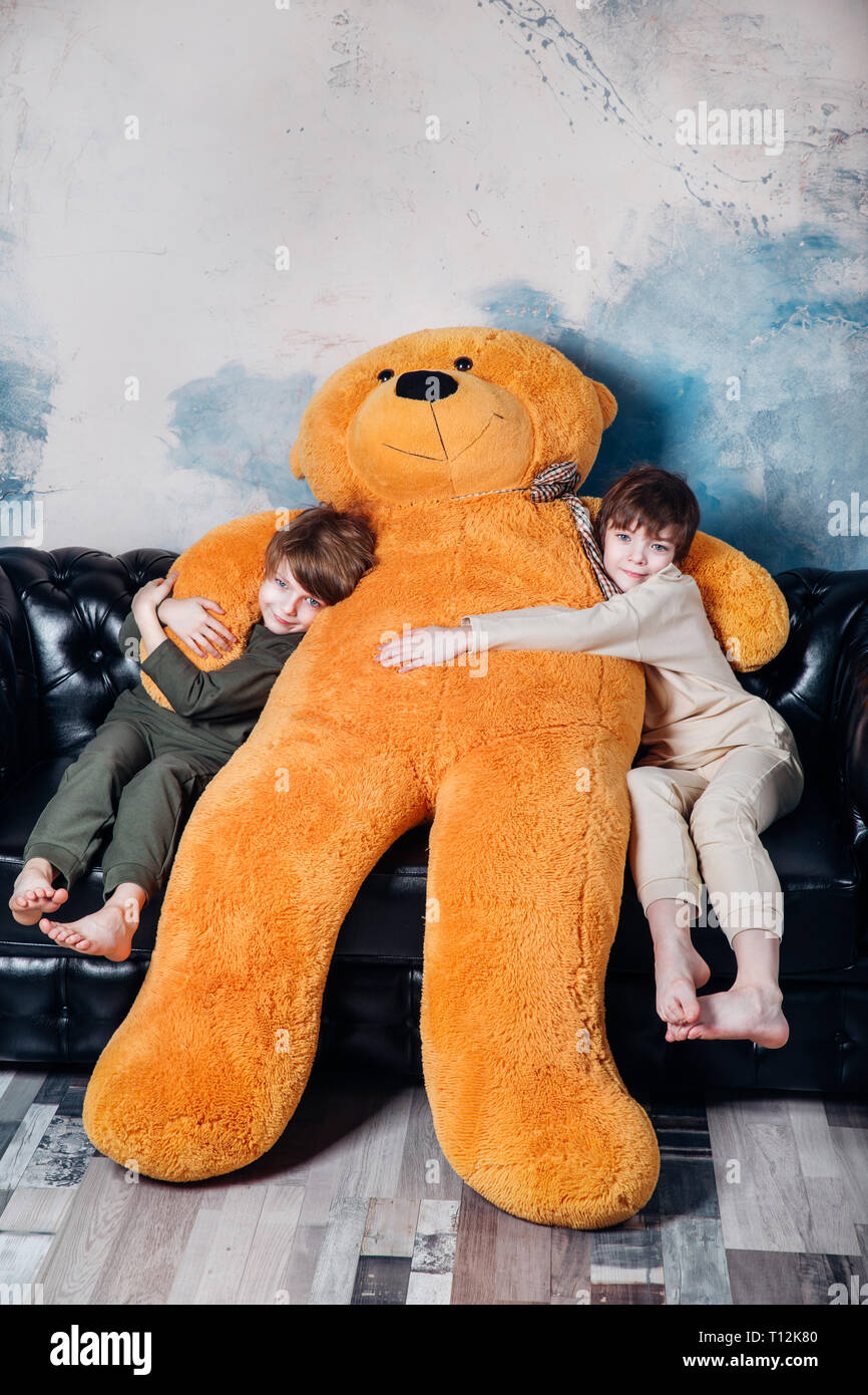 Happy twin brothers in pajamas hugging big teddy bear soft toy happy smiling at home Stock Photo