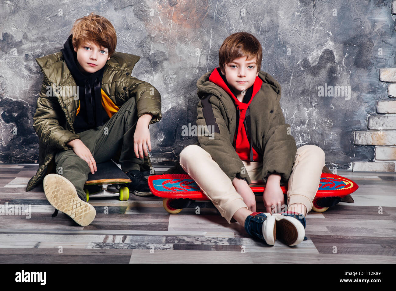 Two little twin boys in casual clothes sitting on skateboard in studio. Teen and kids fashion concept. Stock Photo