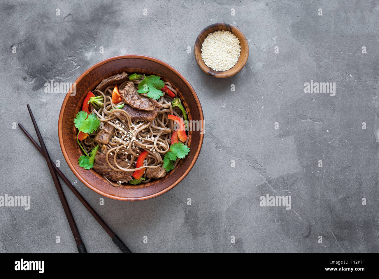 Stir fry with soba noodles, beef and vegetables. Asian healthy food, stir fried meal in bowl on dark background, top view, copy space. Stock Photo