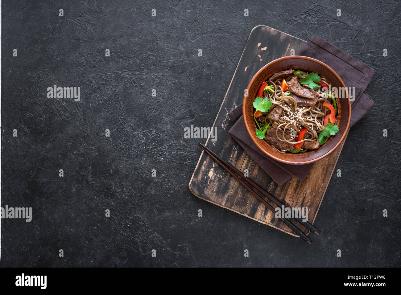 Stir fry with soba noodles, beef and vegetables. Asian healthy food, stir fried meal in bowl on black background, top view, copy space. Stock Photo