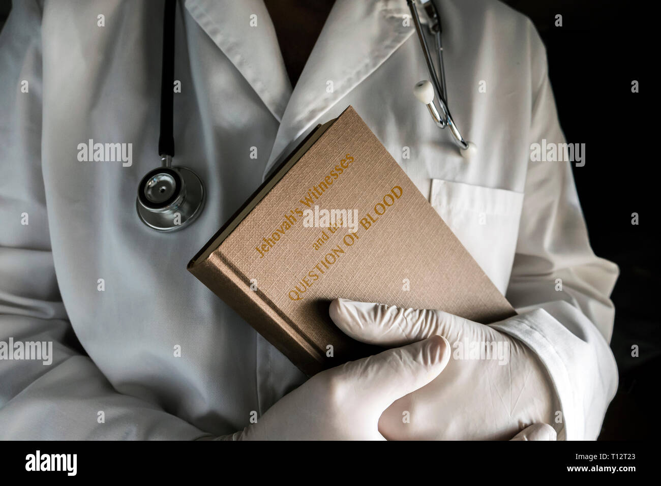 Doctor holds book Jehovah's Witnesses and the Question of Blood, concept of denial of blood transfusions, conceptual image, horizontal composition Stock Photo