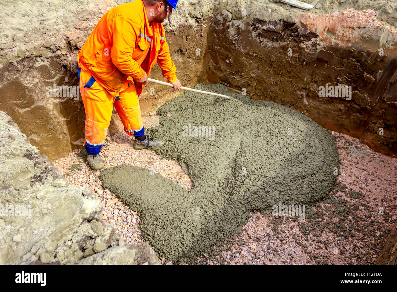 Mason is using rake to spreading fresh concrete in square trench Stock ...