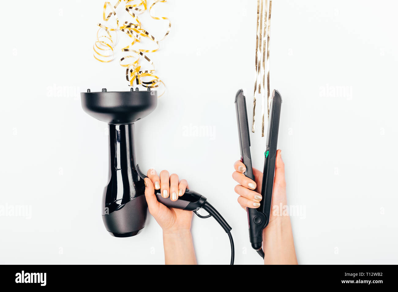 Creative concept of comparing styling of curly and straight hair. Female's hands holding hairdryer and straightener next to stylized gold strands on w Stock Photo