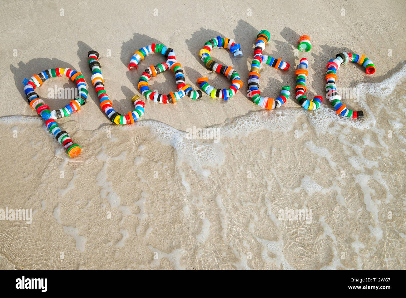Plastic awareness message made from discarded bottle caps in a colorful word on the shore of a smooth beach Stock Photo