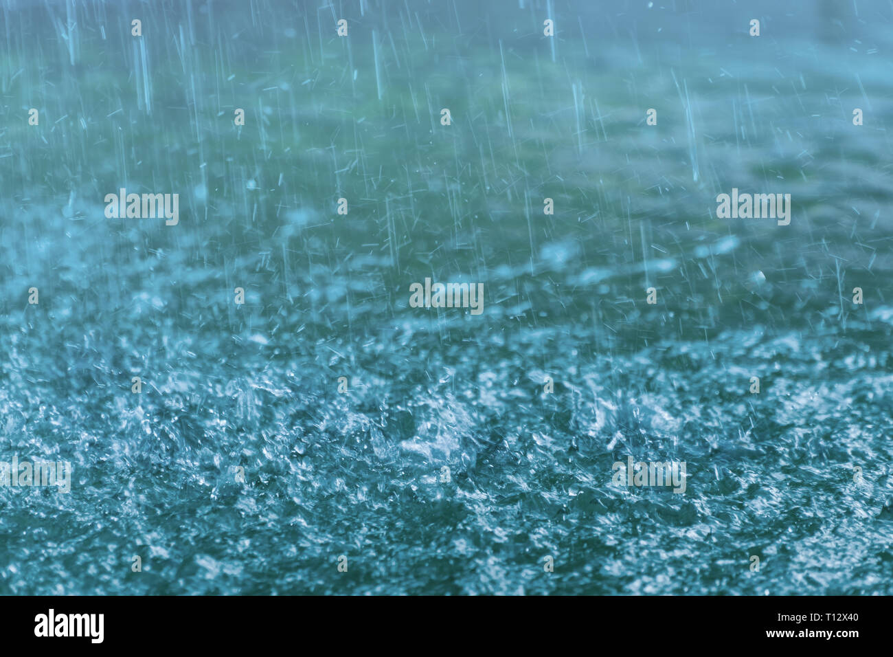 Droplets hitting water surface. Raindrops falling on the blue surface of water.  Motion blur. Stock Photo