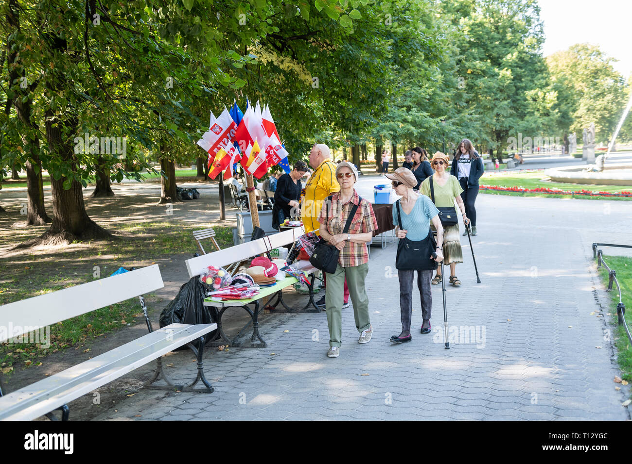 Warsaw, Poland - August 23, 2018: People local woman vendor selling souvenirs Polish EU European Union flags on bench in summer Saxon Gardens Park Stock Photo