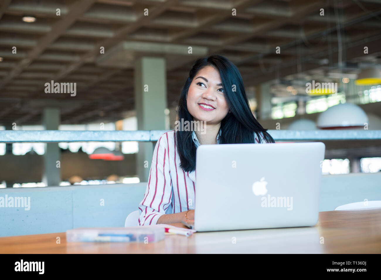 A young south east asian woman sits at a table in a modern university ...