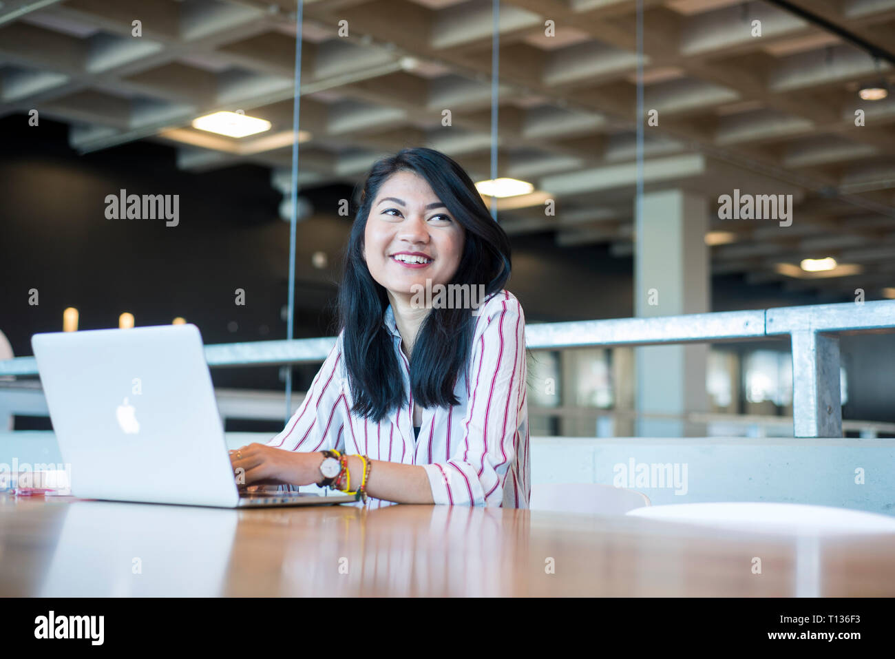 A young south east asian woman sits at a table in a modern university ...