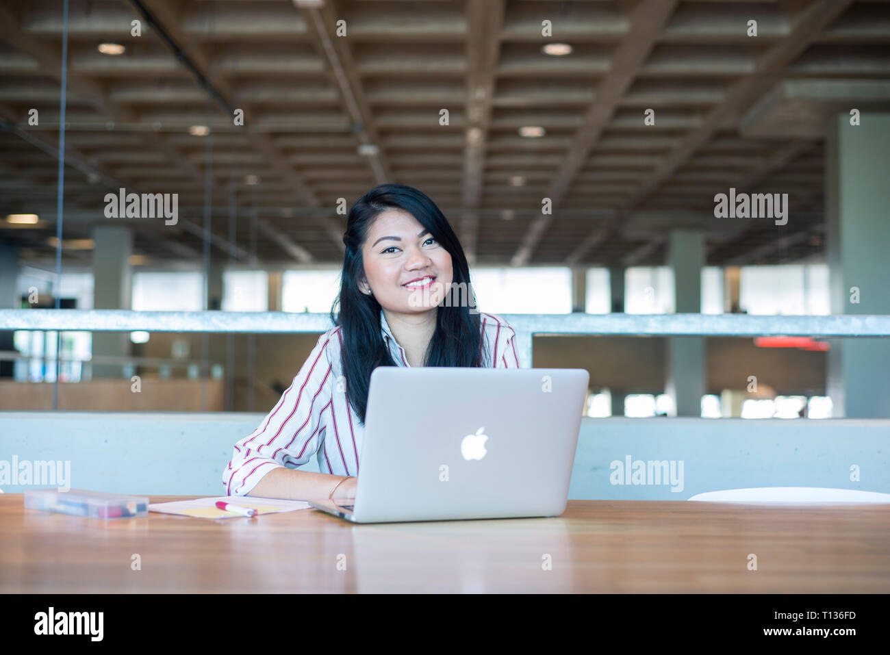 A young south east asian woman sits at a table in a modern university ...