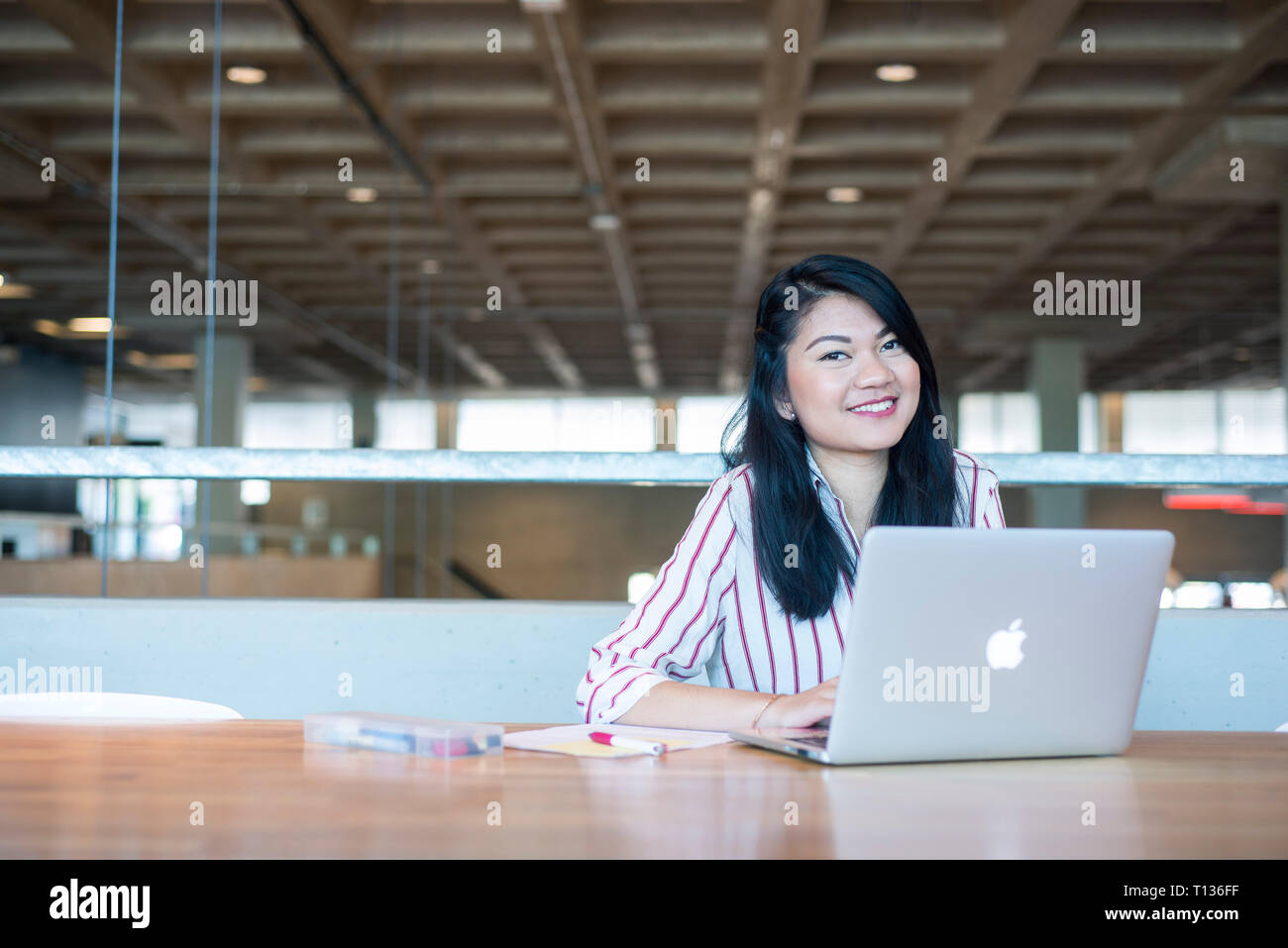 A young south east asian woman sits at a table in a modern university ...