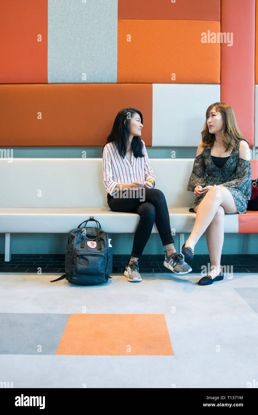 Two young south east asian students sitting and chatting on campus Stock Photo