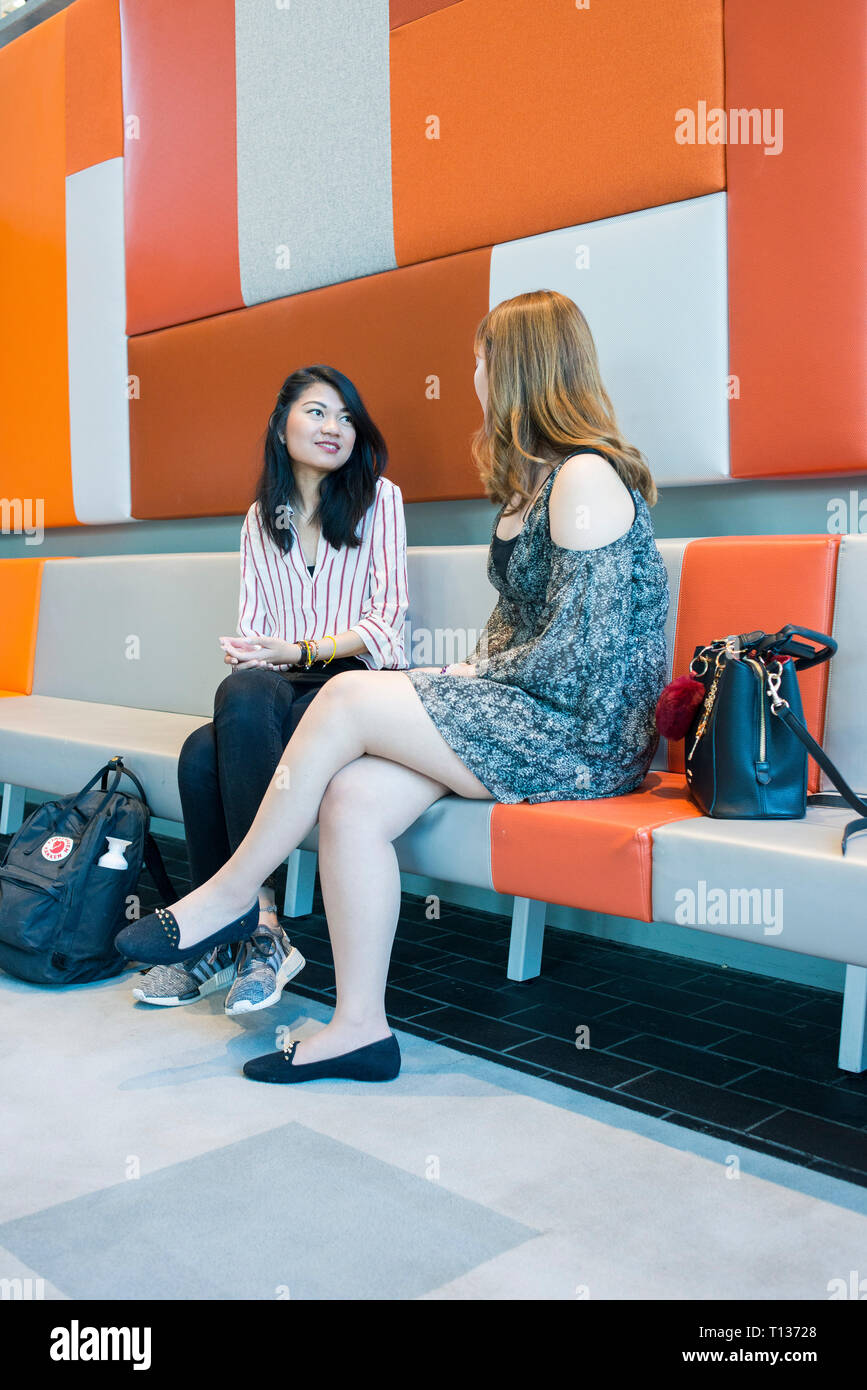Two young south east asian students sitting and chatting on campus Stock Photo