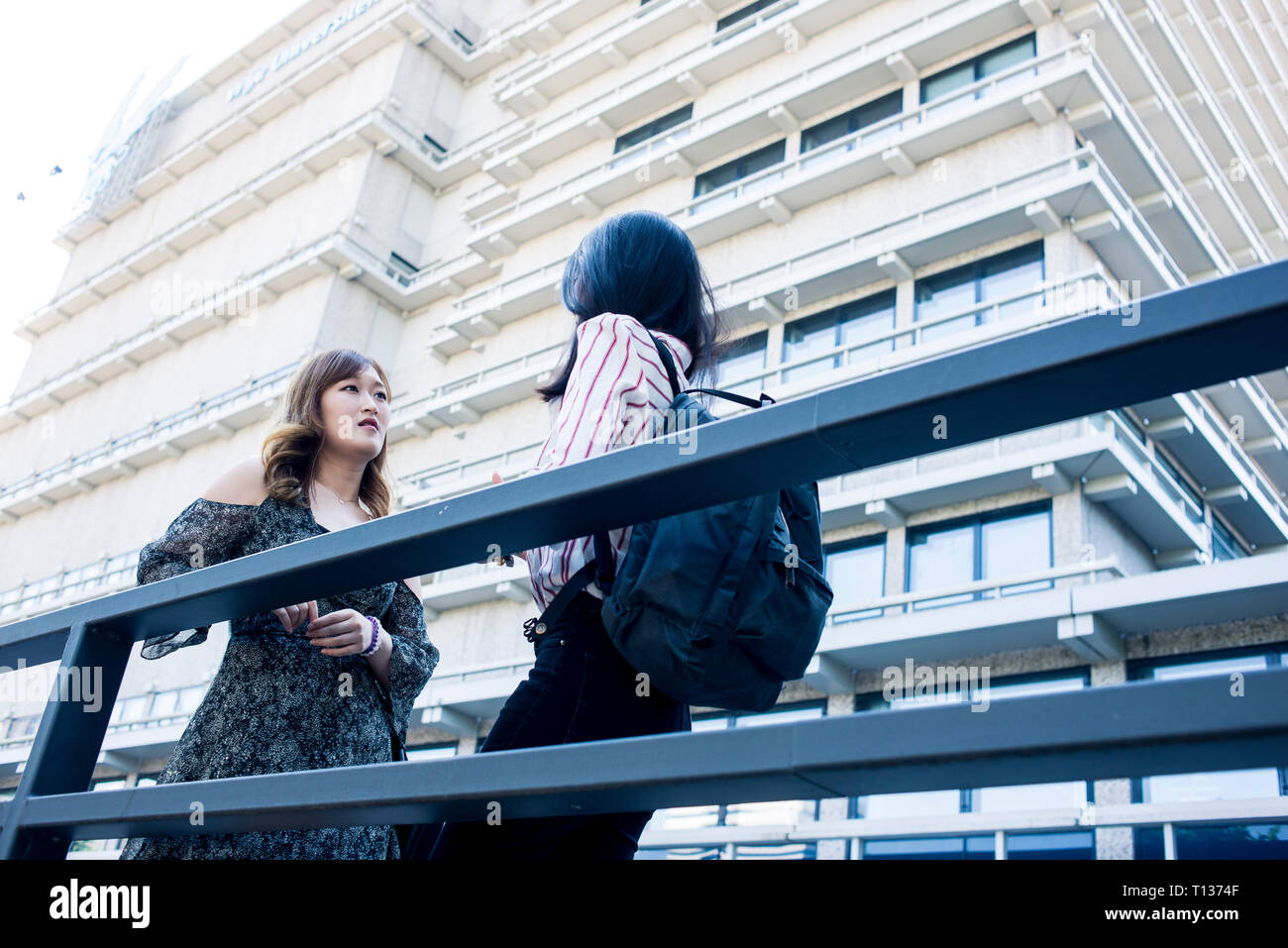 Two young female students stand outside their college modern buildings ...