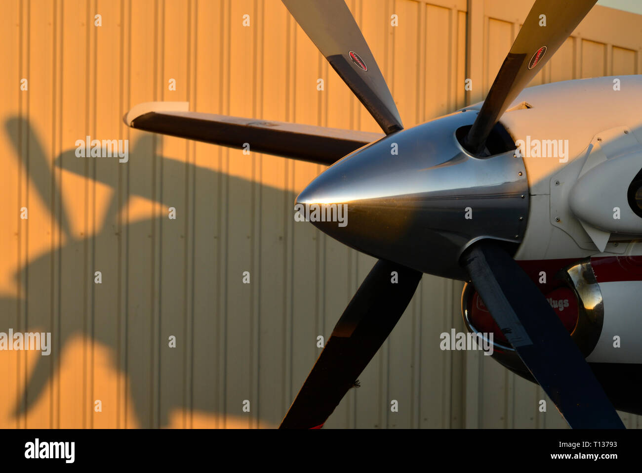 The nose of a Pilatus PC12 outside an aircraft maintenance hangar. Sunlight illuminates the building. Stock Photo
