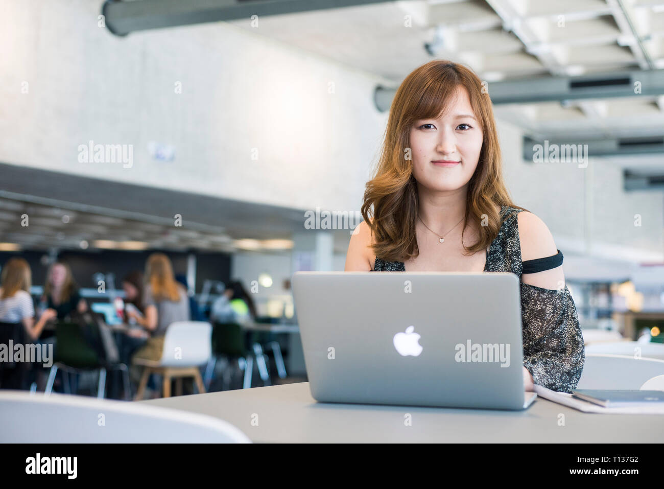 A young south east asian woman sits at a table in a modern university ...
