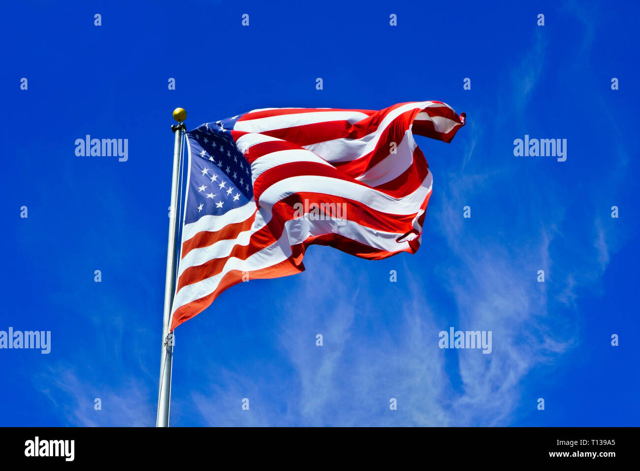 Beautiful US American flag in bold colors. USA flag with stars and stripes against a blue sky background with very decorative clouds passing by. Stock Photo