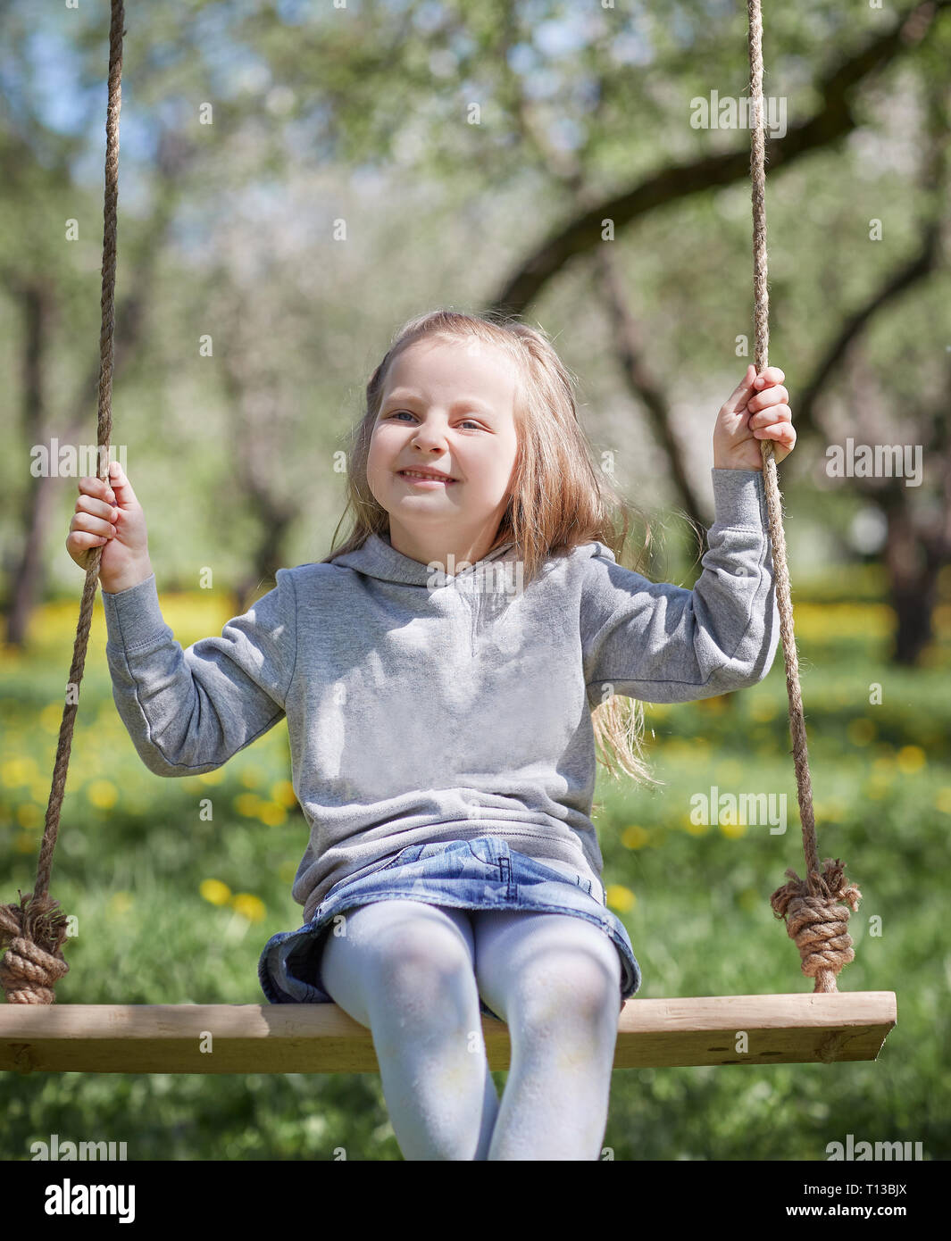 smiling little girl sitting on a swing in the garden Stock Photo - Alamy