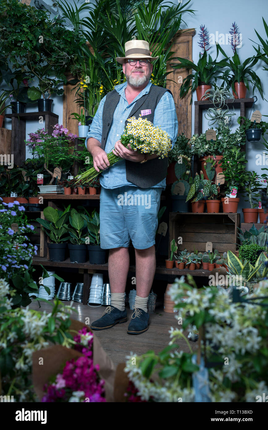 A male small business owner stands in his florist shop holding a bunch of flowers. Stock Photo