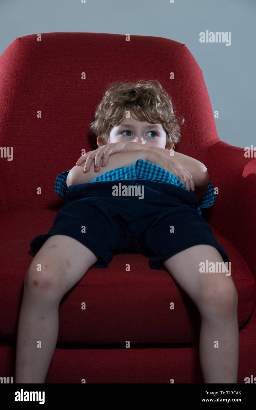 a board young white boy being restless and fed up on a colourful sofa Stock Photo
