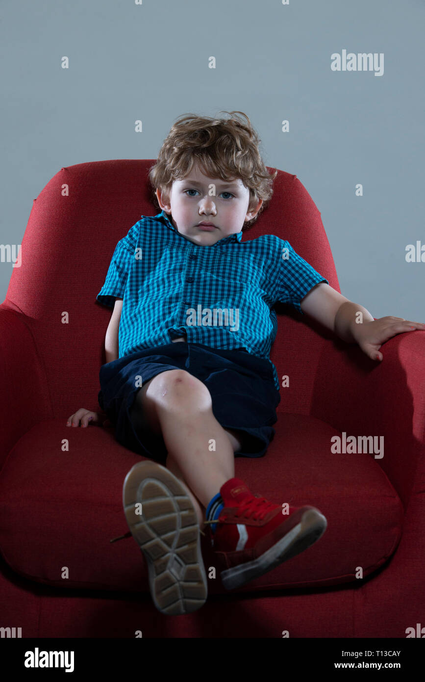 a board young white boy being restless and fed up on a colourful sofa Stock Photo