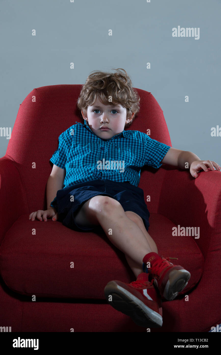 a board young white boy being restless and fed up on a colourful sofa Stock Photo