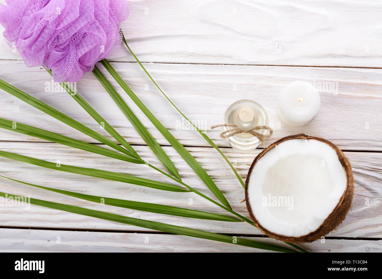 Flat lay Coconut oil in glass bottle bath sponge candle and shell pieces on white wooden table Stock Photo