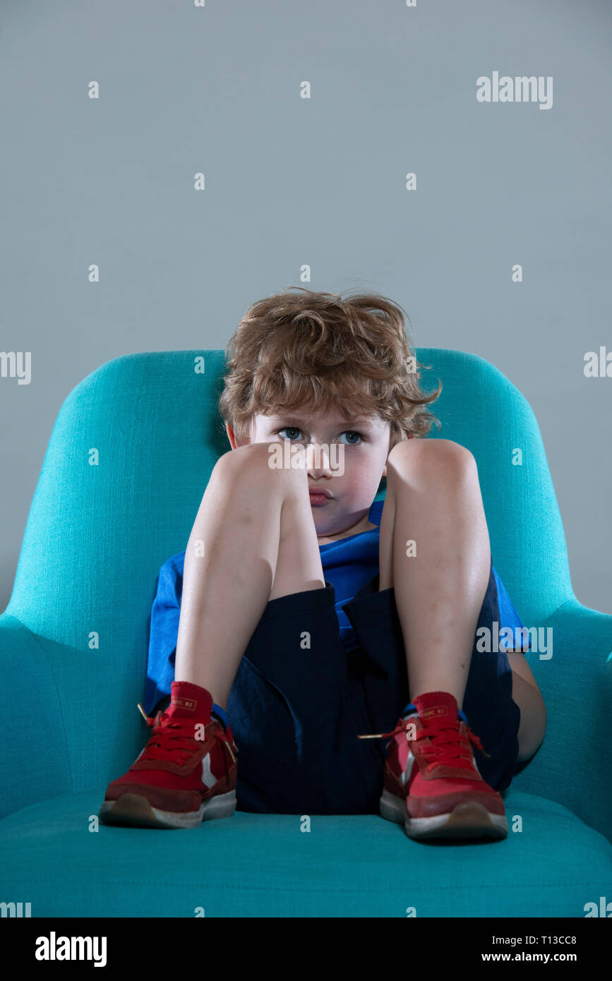a board young white boy being restless and fed up on a colourful sofa