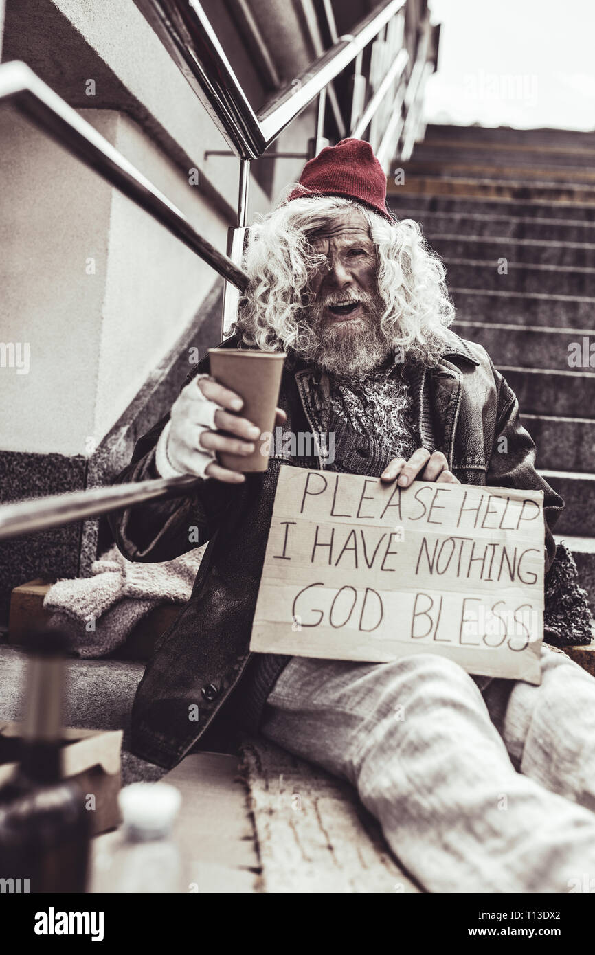 Desperate beggar sitting outside and writing poster asking for help. Stock Photo