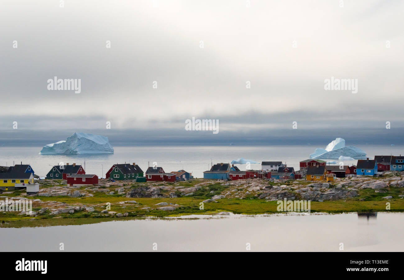 Floating iceberg and brightly painted houses along the shore, Qeqertarsuaq, Greenland Stock Photo