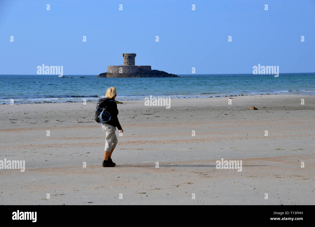 Woman Hiker Walking on the Beach near La Rocco Tower on an Tidal Island in St Ouen's Bay on the Island of Jersey, Channel Isles, UK. Stock Photo