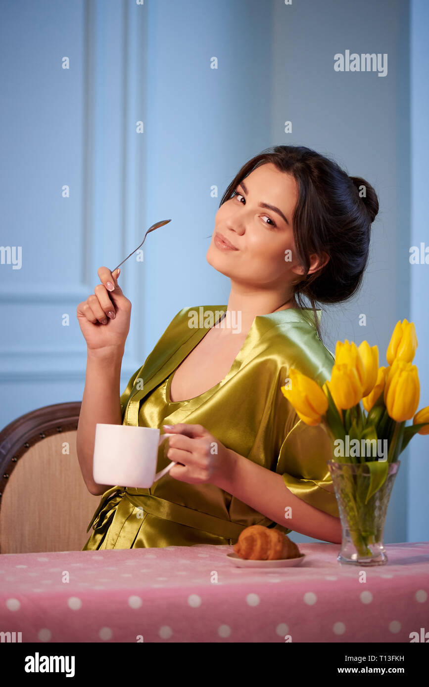 Beautiful young woman in sleepwear drinking morning coffee with croissants. Stock Photo