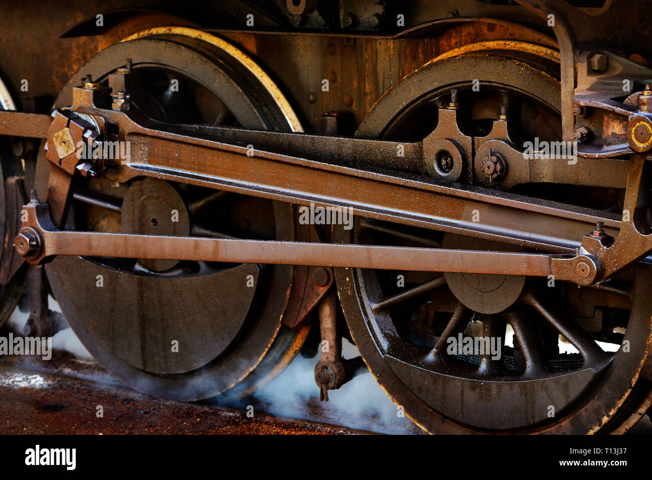 Close up of a restored steam locomotives counterbalanced main driving wheels, with steam issuing. Western Australia. Stock Photo
