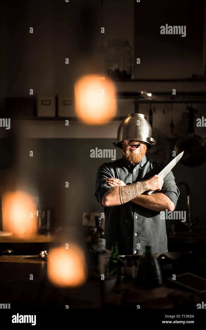 Man with kitchen knife standing in kitchen, wearing colander as helmet Stock Photo Alamy