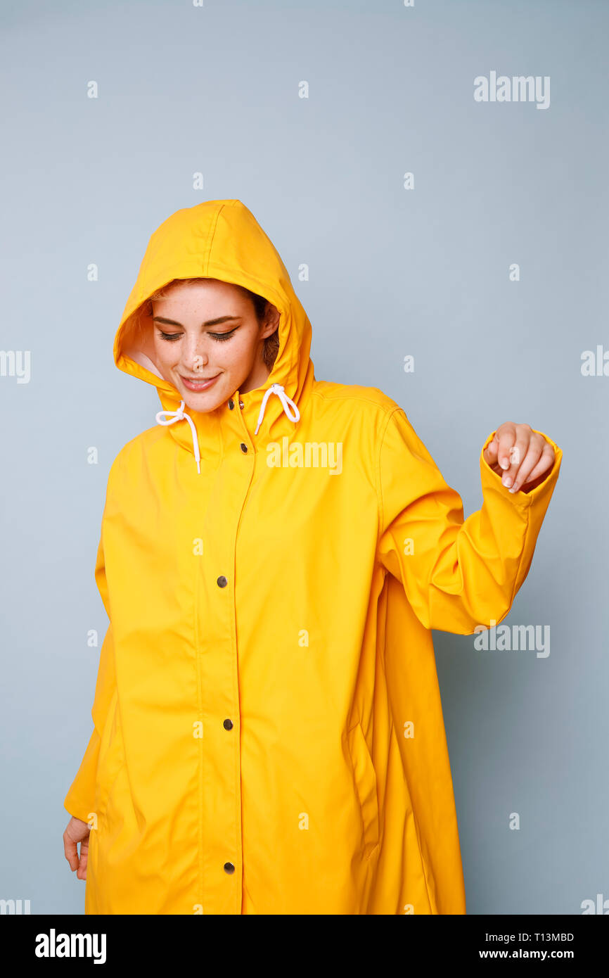 Smiling young woman wearing yellow rain coat in front of blue ...