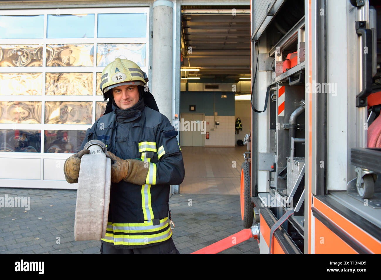 Portrait of firefighter at fire engine holding firehose Stock Photo